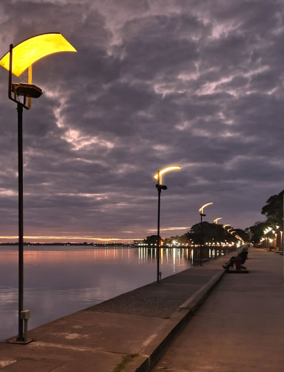 Atardecer sobre la costanera de Chascomús con sus tradicionales luminarias amarillas encendidas reflejándose en el agua.