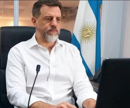 Diego Kravetz sentado ante una computadora con una bandera argentina detrás